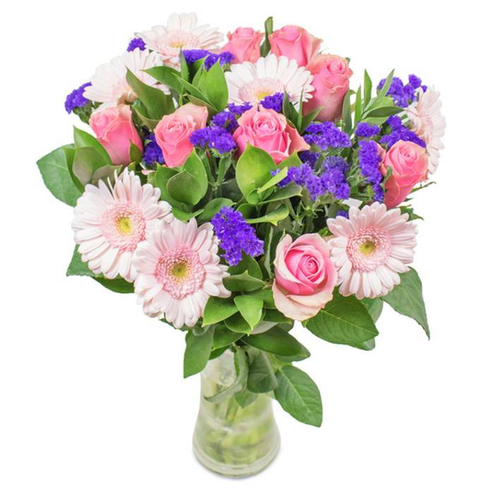 A vibrant, expertly arranged bouquet from Deptford Flowers sits gracefully in a clear glass vase, set against a pristine white backdrop that accentuates its colours. At the core, 7 to 9 pink roses display their elegant, classic spiral forms-some still tightly closed, others just unfurling. These are complemented by 5 to 7 gently radiant pale pink gerbera daisies, each with large, circular heads and layers of delicately ruffled petals, anchored by soft, almost white centers that seem to glow. Sprigs of vivid purple statice weave between the main blossoms, infusing the design with bold contrast and modern flair, much like the lively markets along Deptford High Street. Lombardy-inspired foliage, deep green and full, creates an abundant, fresh base. The crystal vase reveals each stem and a pool of clear water, reflecting the bouquet's natural charm and vitality. Available for same-day delivery from Deptford Flowers, this arrangement is perfect for birthdays, anniversaries, or as a stylish accent in homes and studios by the river, expressing joy, affection, and the welcoming spirit of SE8.